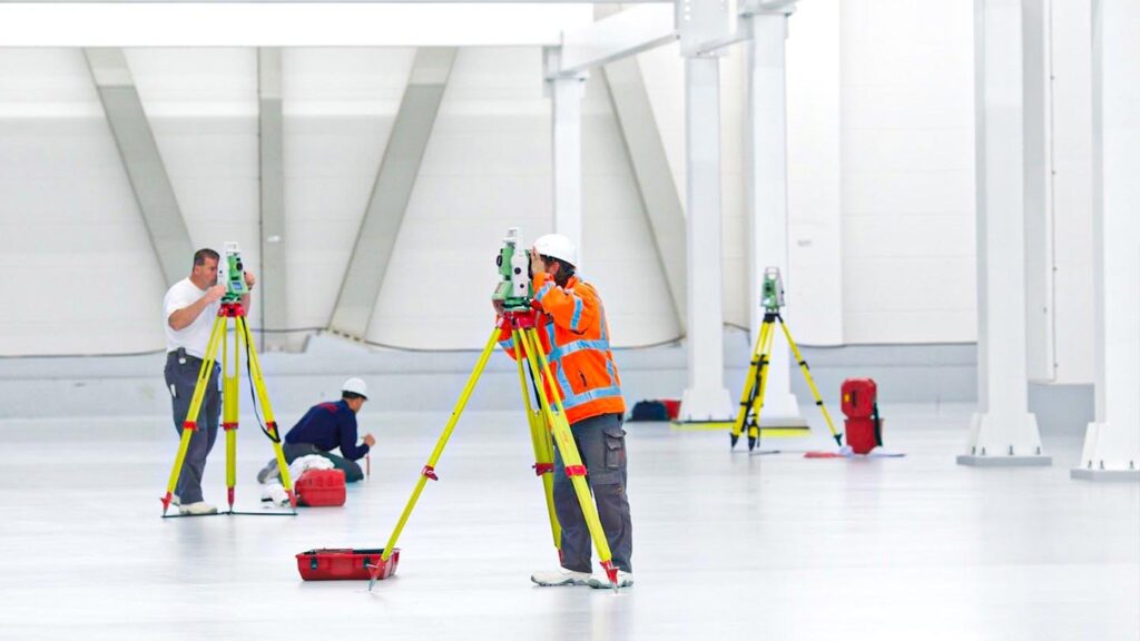 Maatvoerders voeren bouwmaatvoering uit met total stations in een bedrijfshal voor nauwkeurige plaatsing van constructies.